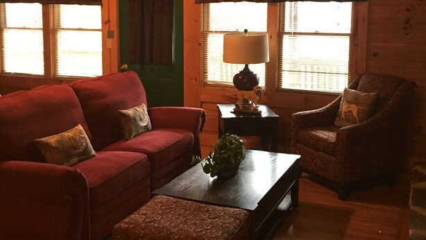 A cozy living room with a red sofa, a patterned ottoman, a wooden coffee table, and a lamp.