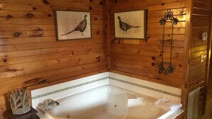 A wooden cabin with a large bathtub, framed pictures of birds, and a decorative metal fixture.