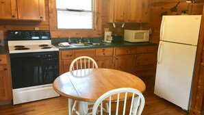 A wooden kitchen with a stove, microwave, refrigerator, and a dining table with chairs.