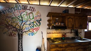 Une cuisine avec des meubles de rangement en bois, une cuisinière à gaz et un mur orné d’un graffiti représentant un arbre.