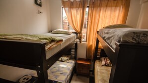 Une chambre de dortoir avec des lits superposés, une petite table de chevet et une fenêtre avec des rideaux.
