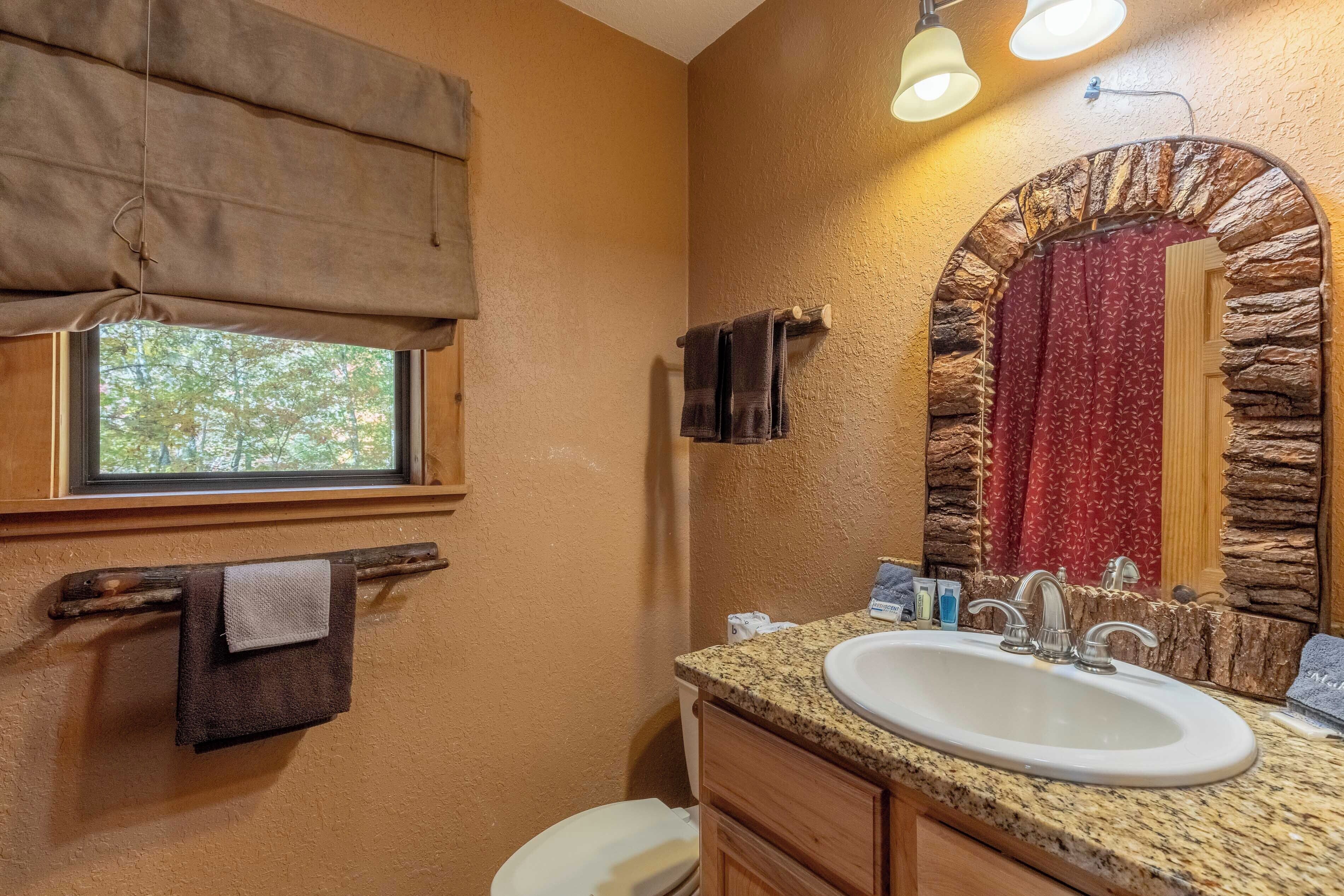 A bathroom with a stone arch mirror, a granite countertop sink, and a window with a beige blind.