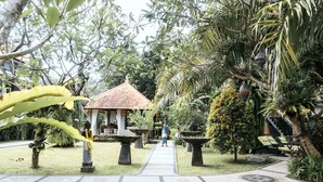 Caminho de jardim que leva a um gazebo com telhado de azulejos, cercado por vegetação exuberante e palmeiras.