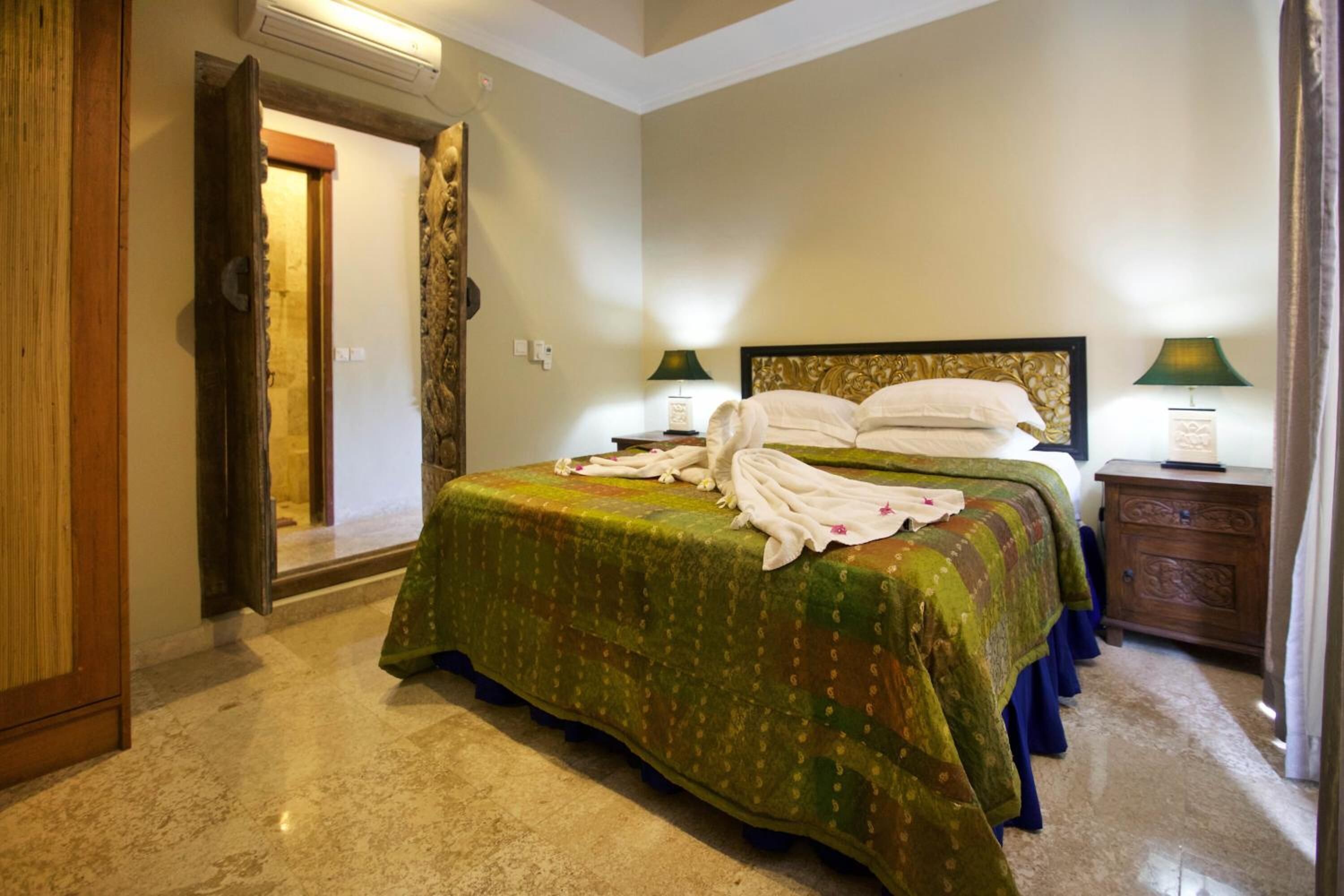 A hotel room with a bed, two bedside tables, a wooden wardrobe, and a door leading to another room.