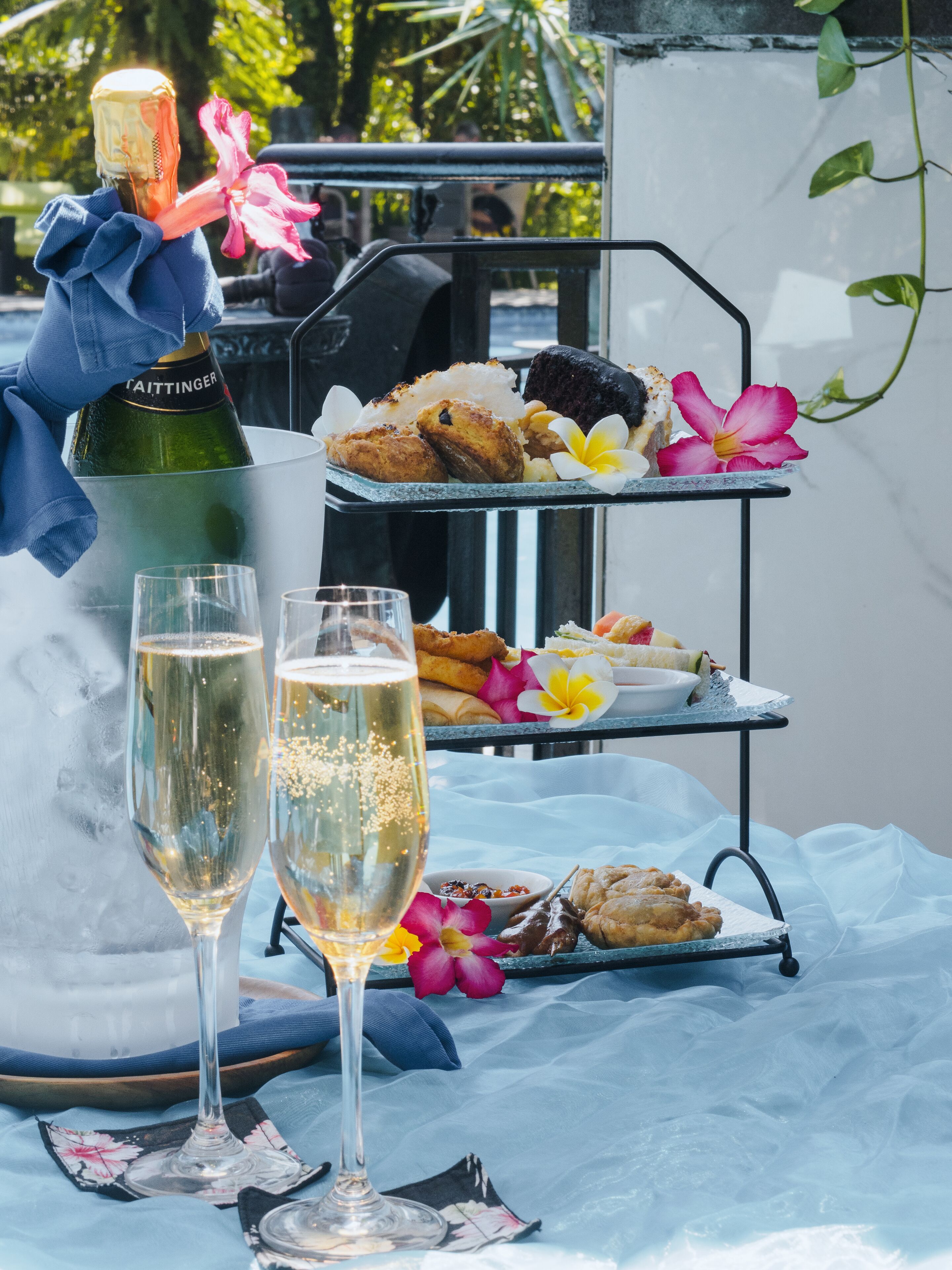 Una mesa con dos copas de champán, una botella de champán y una bandeja de postres con pasteles y flores.