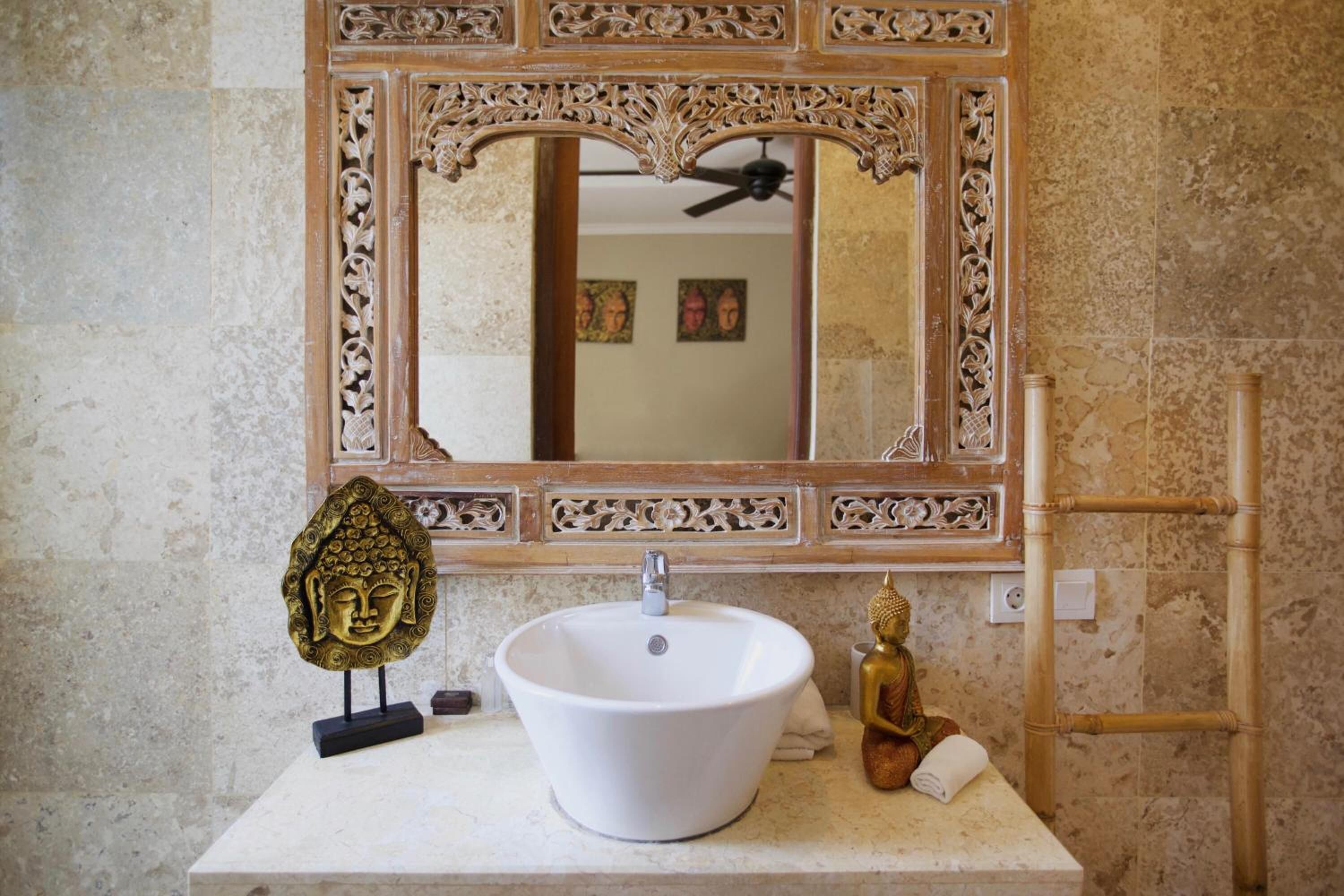 A bathroom with a white sink, ornate mirror, and decorative Buddha statue.