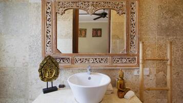 A bathroom with a white sink, ornate mirror, and decorative Buddha statue.