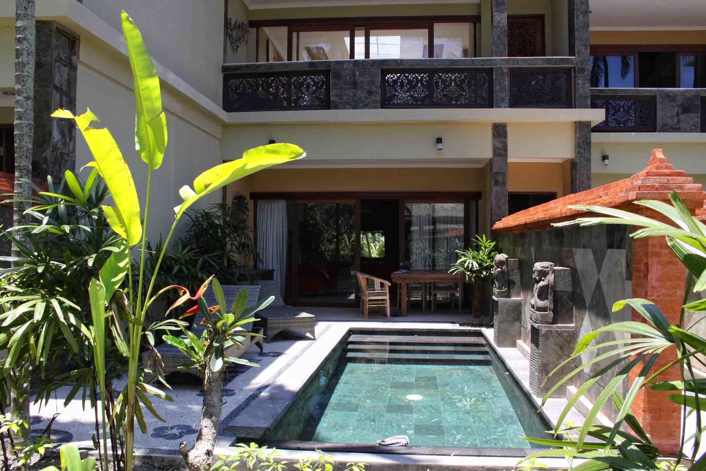 Un edificio a due piani con piscina, area relax esterna e piante tropicali.