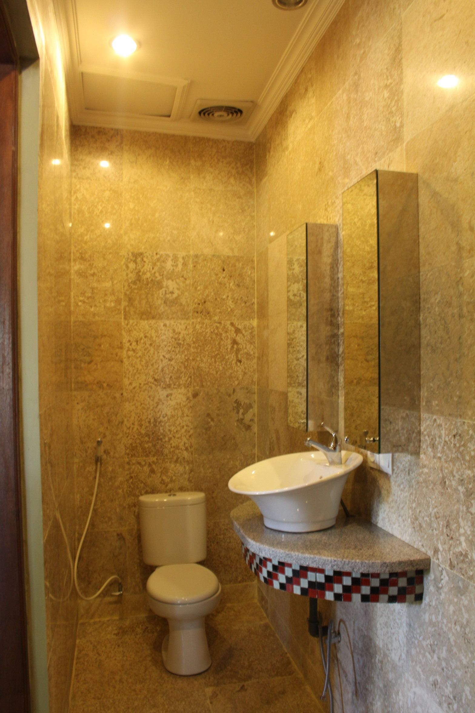 A bathroom with a marble wall, a toilet, a sink with a mirror, and a shower area.