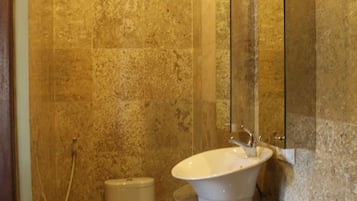 A bathroom with a marble wall, a toilet, a sink with a mirror, and a shower area.