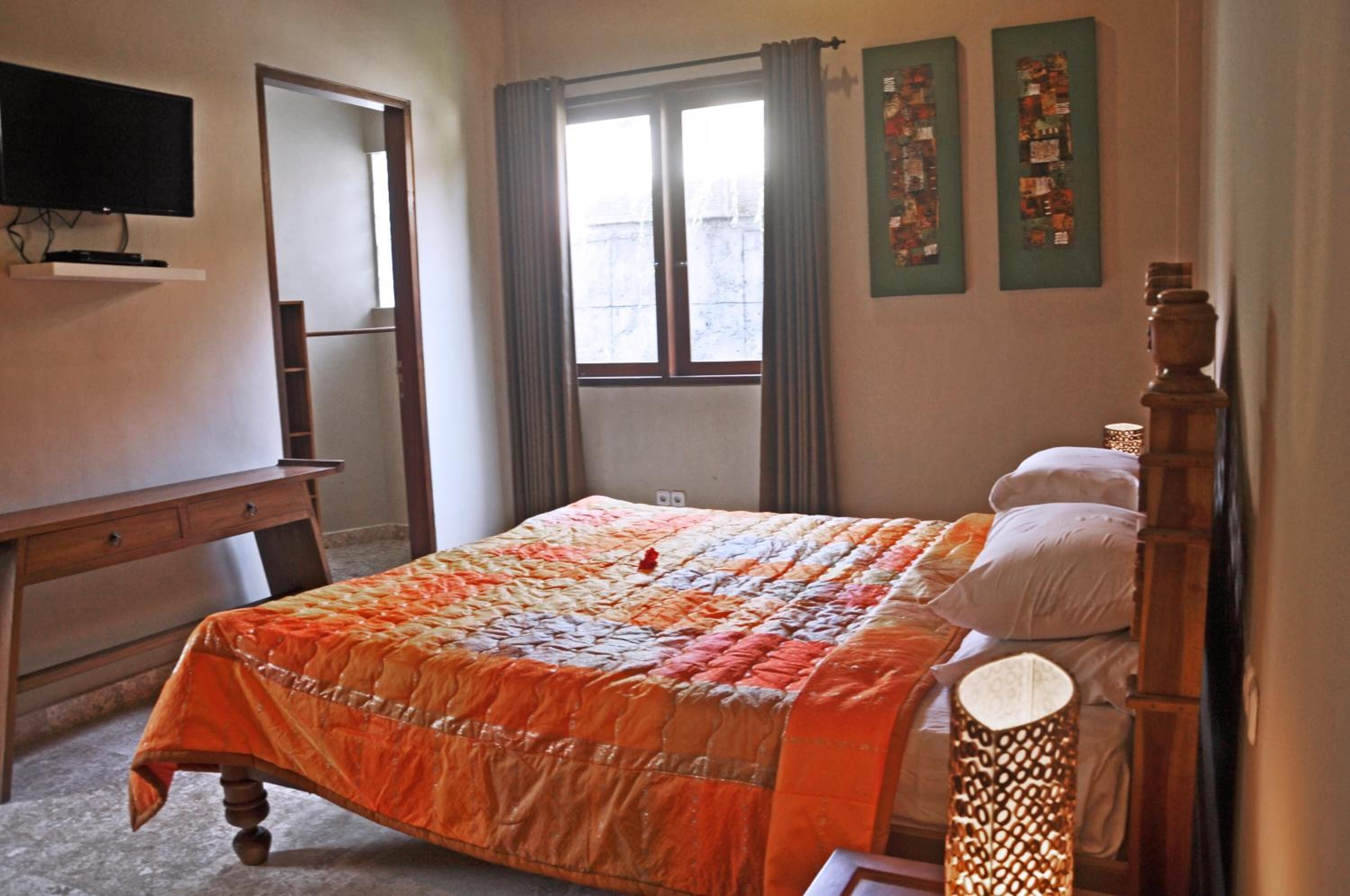 A bedroom with a bed, a wooden desk, a television, and a window with curtains.