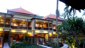 Um hotel com vários andares, telhado de telhas vermelhas, varandas e um jardim bem cuidado com palmeiras.