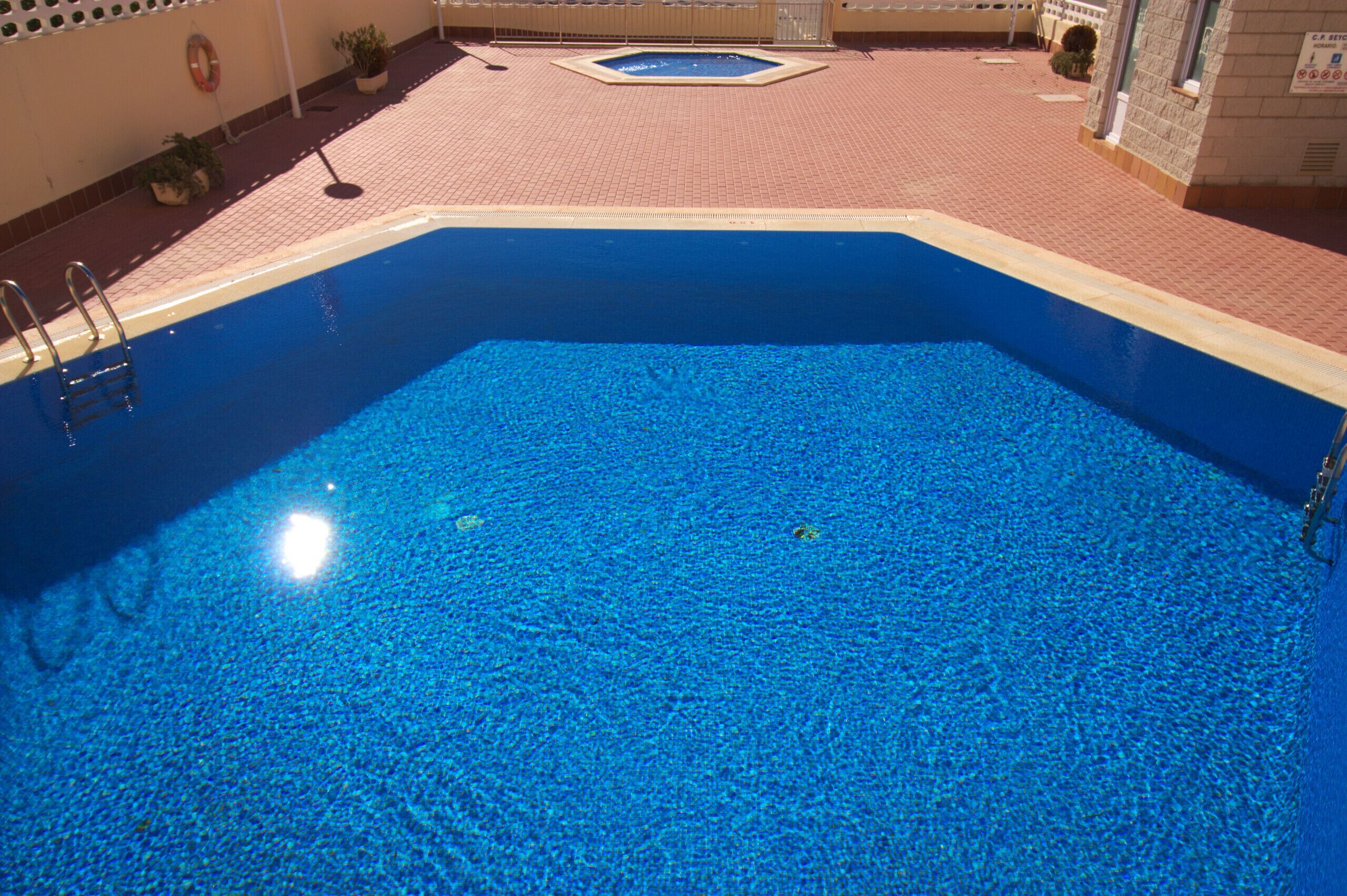 Ein Schwimmbecken mit glasklarer, blauer Wasseroberfläche, umgeben von einer gefliesten Liegefläche.