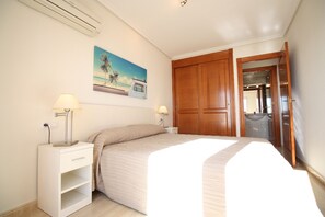 A bedroom with a bed, bedside lamps, a nightstand, a wooden wardrobe, and a painting of a beach scene. - 6th floor, front line facing the Mediterranean (La Manga del Mar Menor)