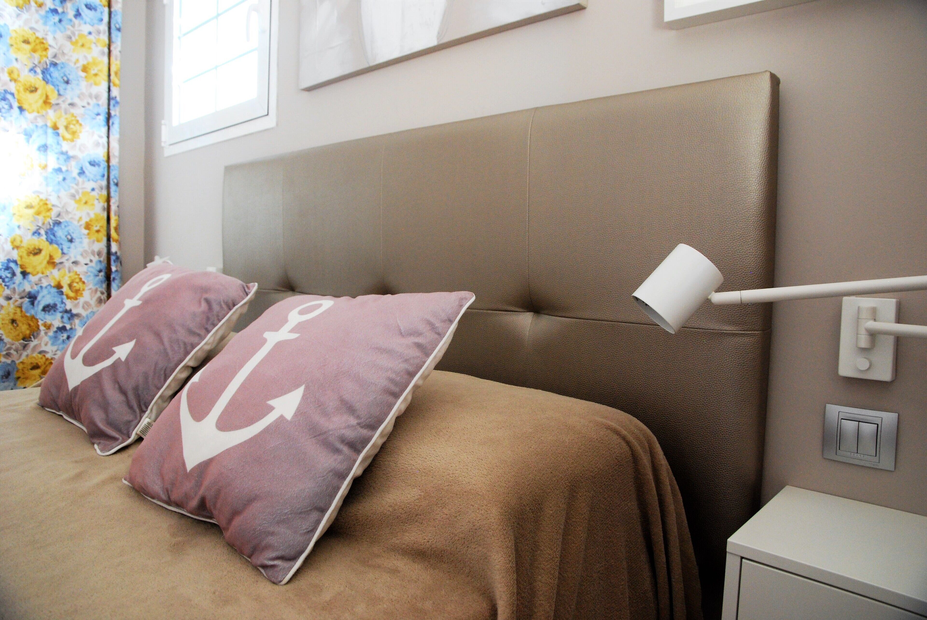 A bedroom with a large bed, two pillows with anchor designs, a bedside lamp, and a nightstand.
