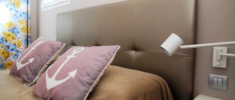 A bedroom with a large bed, two pillows with anchor designs, a bedside lamp, and a nightstand.