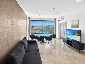 Un salon moderne comprenant un canapé, une table à manger, des chaises, un téléviseur à écran plat et une vue sur la ville grâce à de grandes fenêtres.