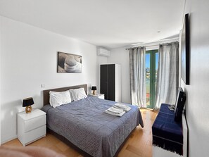 Ein Hotelzimmer mit Bett, Nachttischen, einem Kleiderschrank, einem Fernseher und Blick durch die Vorhänge.