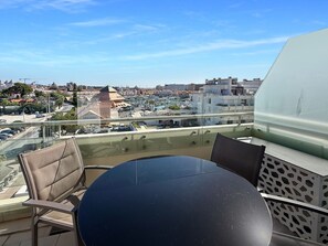 Ein Balkon mit Glasgeländer, einem runden Tisch und zwei Stühlen.