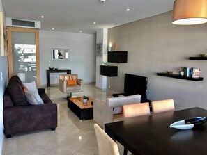 A modern living room with a sofa, armchairs, a coffee table, a TV, and a dining table.