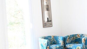 Une pièce avec un mur blanc, un tableau encadré représentant un phare et un canapé bleu à motifs floraux.