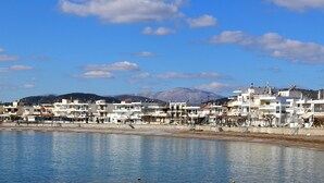 A coastal town with modern buildings, a beach, and mountains in the background.