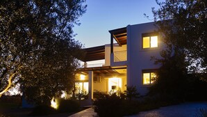 A modern two-story house with a covered patio, a visible kitchen area, and a paved driveway.