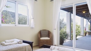 A bedroom with two beds, a wicker chair, and a large sliding glass door leading to an outdoor area.