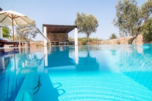 En klarblå pool med en hoppställning, solstolar och en stenmur i bakgrunden.