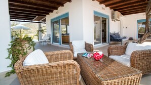 A covered outdoor seating area with wicker furniture and a glass table, overlooking a scenic landscape.