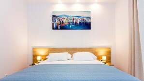 Habitación de hotel con una cama grande, cabecera de madera, dos lámparas de noche y un cuadro sobre la cama.