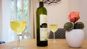 Una botella de vino, dos copas de vino y un florero con una rosa y esferas decorativas sobre una mesa de madera.