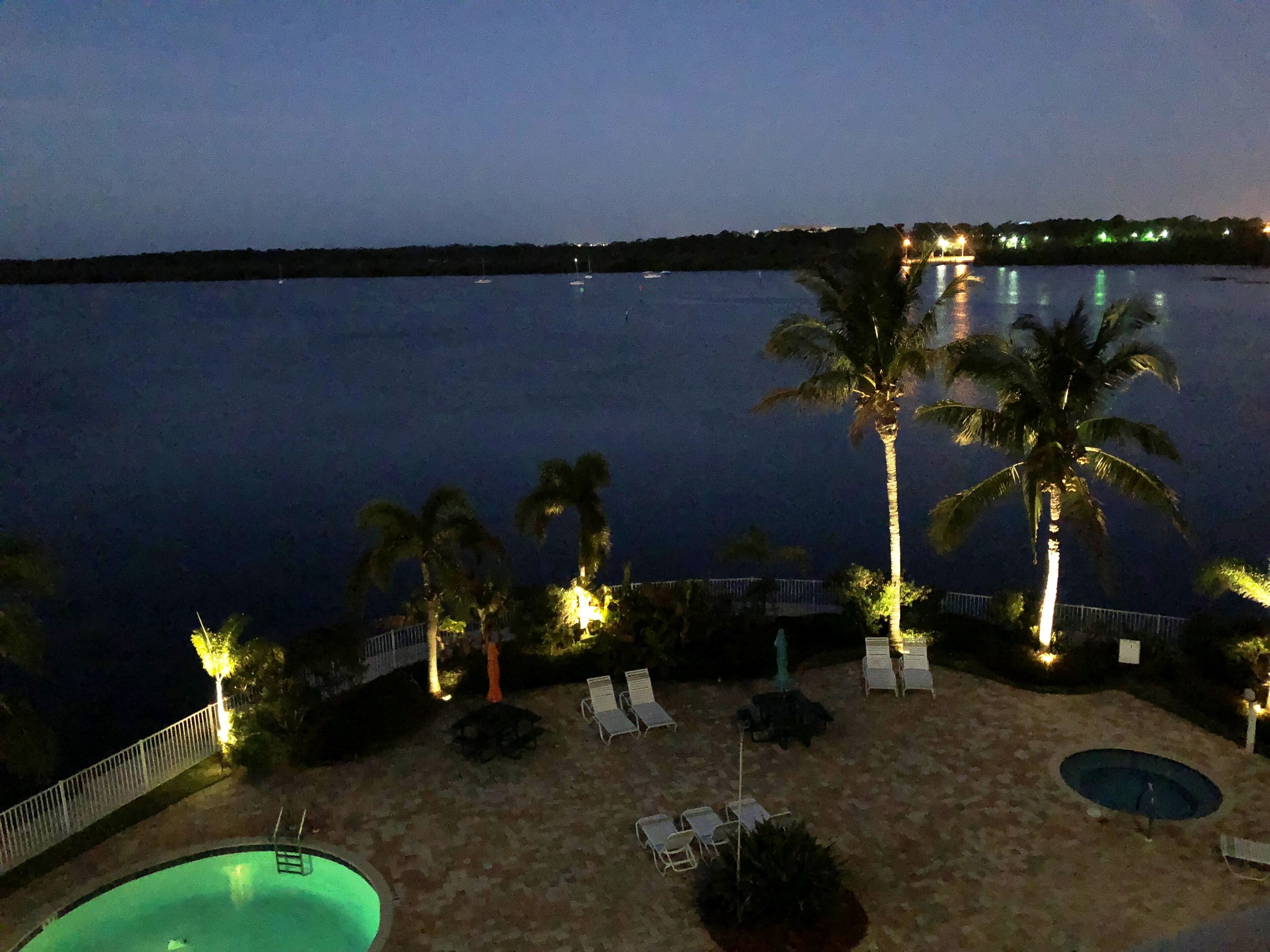 A nighttime view of a beach with a pool, palm trees, and lounge chairs.