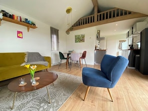 A living room with a sofa, a blue armchair, a coffee table, and a dining area with chairs and a table. - Modern chalet situated on the edge of the park. This chalet has much to offer for both adults and ch (Burgh-Haamstede)