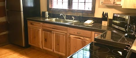 A kitchen with wooden cabinets, a stainless steel refrigerator, a black stove, a sink, and a window with blinds.