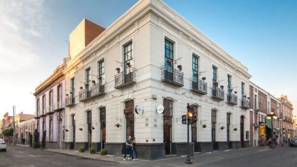 A historic building with a symmetrical facade, multiple balconies, and a corner location. - Meson del Carmen (Puebla)