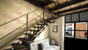 A staircase with wooden steps and metal railings, a grey sofa with cushions, and a window with a view of a brick building. - Meson del Carmen (Puebla)