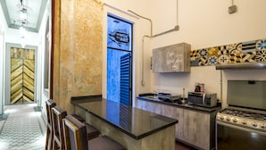 A kitchen with a gas stove, microwave, and a coffee machine. There is a wooden bench and a patterned floor. - Meson del Carmen (Puebla)