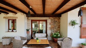 Un patio couvert aménagé avec des meubles en osier, une table carrelée et des plantes en pot.