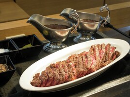 A steak on a plate with two gravy boats beside it.