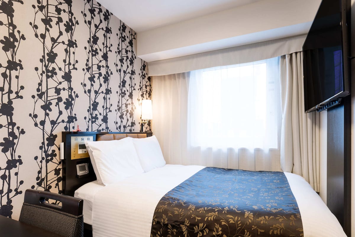 Ein Hotelzimmer mit einem Bett, einem Nachttisch, einer Lampe, einem Fernseher und einem Fenster mit Vorhängen.