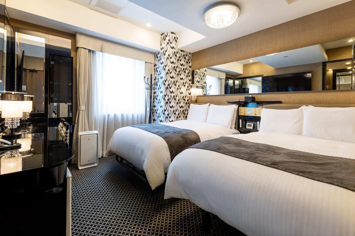 Ein Hotelzimmer mit zwei Betten, einem Schreibtisch mit Telefon, einem Spiegel, einer Kandelaber und einer Wand mit Muster.