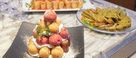 A buffet with various dishes including a pyramid of pastries, a plate of bread, and a dish with a green sauce.