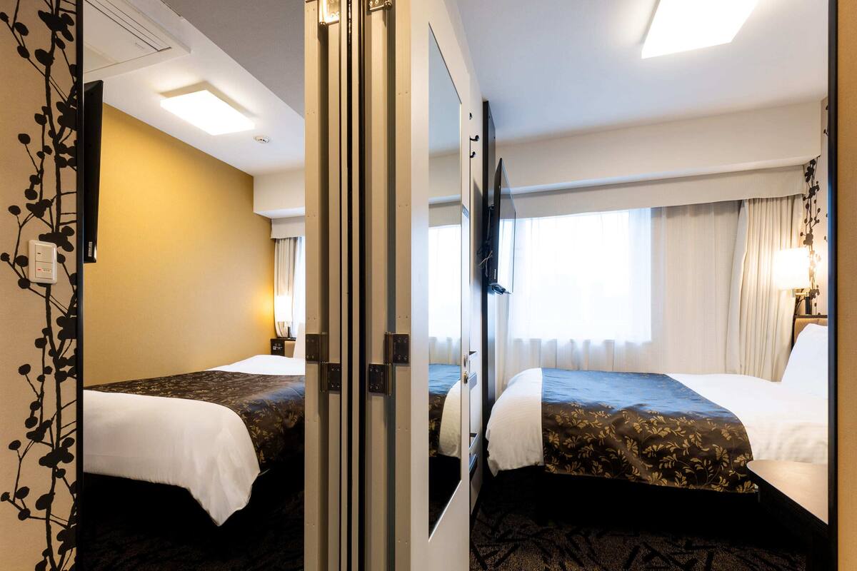 Ein Hotelzimmer mit zwei Betten, einem großen Spiegel, einem Flachbildfernseher und einem Fenster mit Vorhängen.