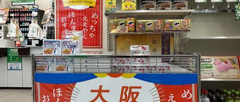 A convenience store with a prominent Osaka Souvenir sign, shelves stocked with snacks, and a Coca-Cola refrigerator.