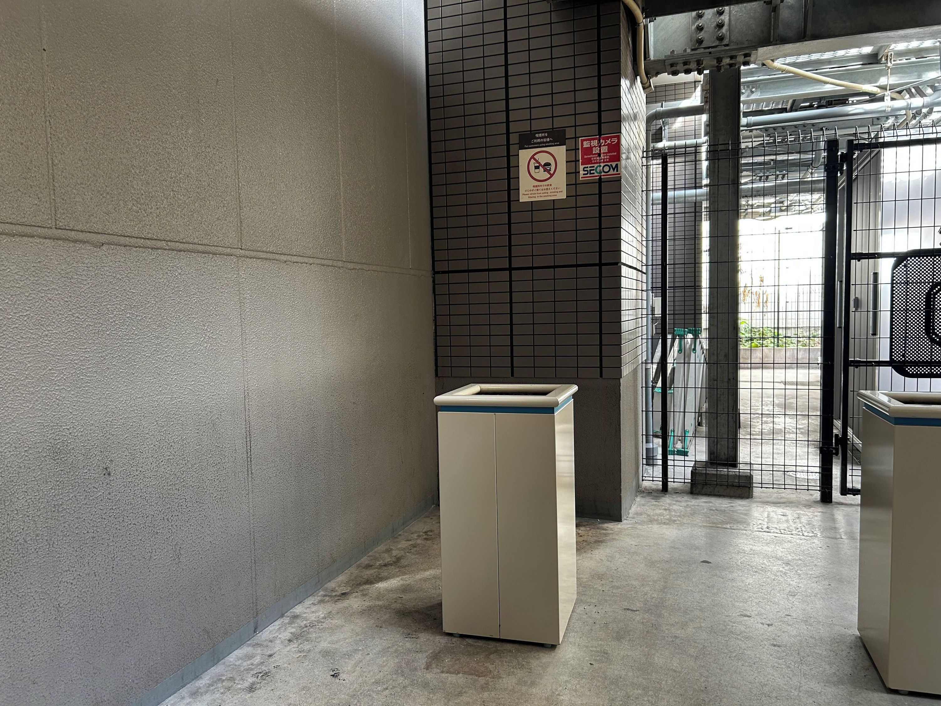 A corridor with a trash bin, a security gate, and a tiled wall.