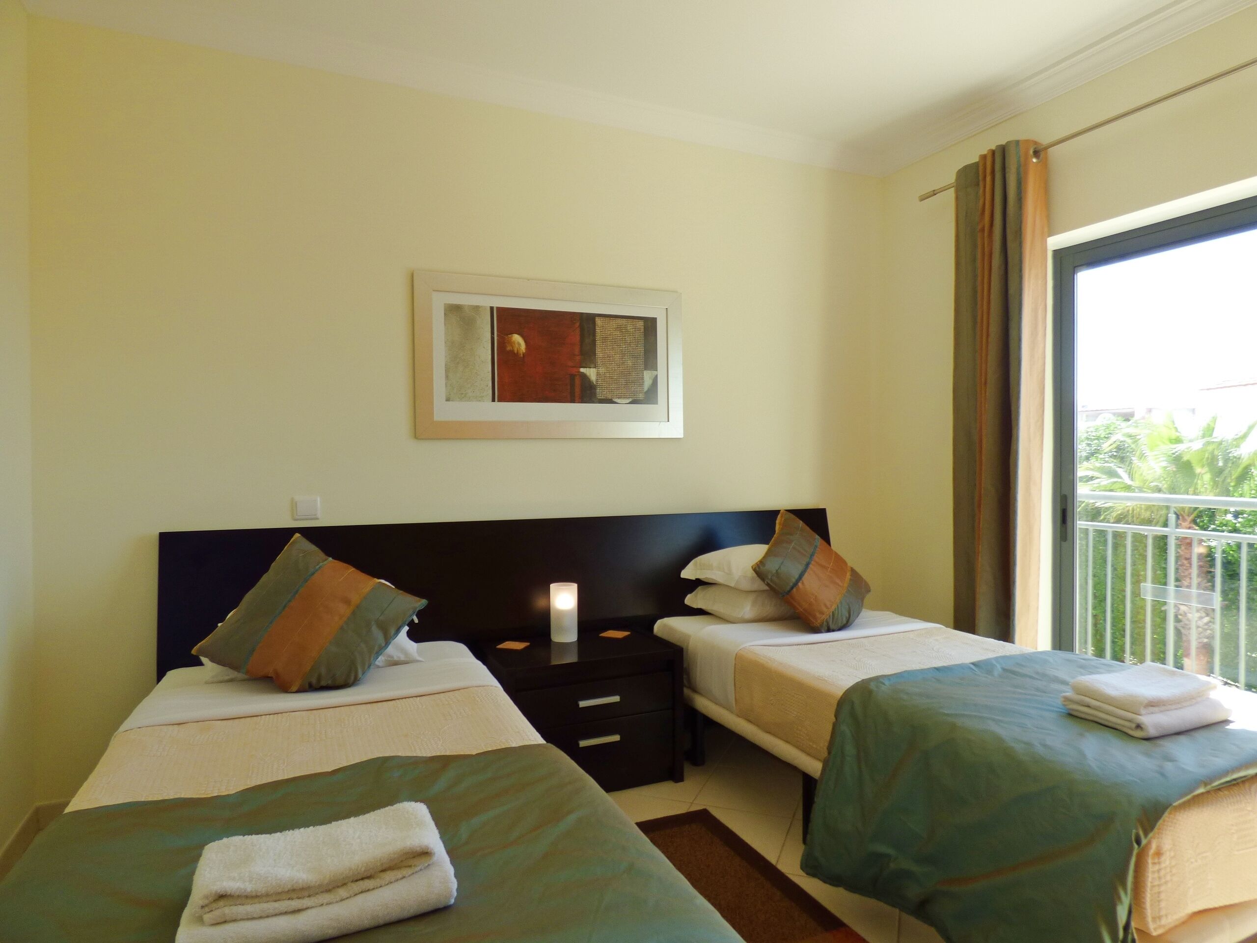 Een hotelkamer met twee bedden, een nachtkastje, een ingelijst schilderij aan de muur en een balkon met een hekwerk.