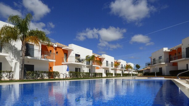 A poolside view of a resort with white and orange buildings, clear blue sky, and palm trees. - 2 Bed House, Pera,  Nr. Albufeira, Algarve. - Shared Pool (PERA)