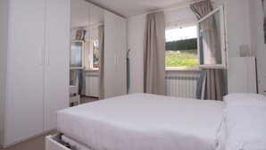 Et soveværelse med seng, skab, et vindue med gardiner og en radiator.