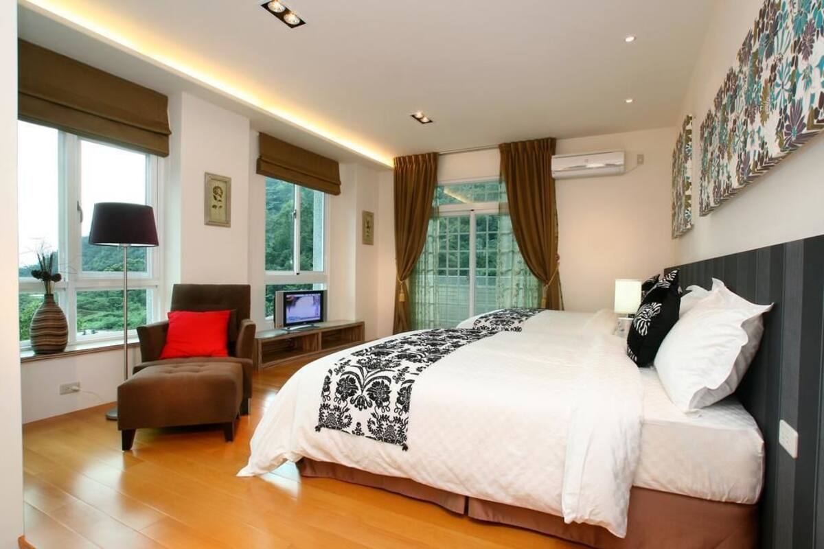 A modern bedroom with a large bed, a desk with a computer, a chair, and a window with curtains.